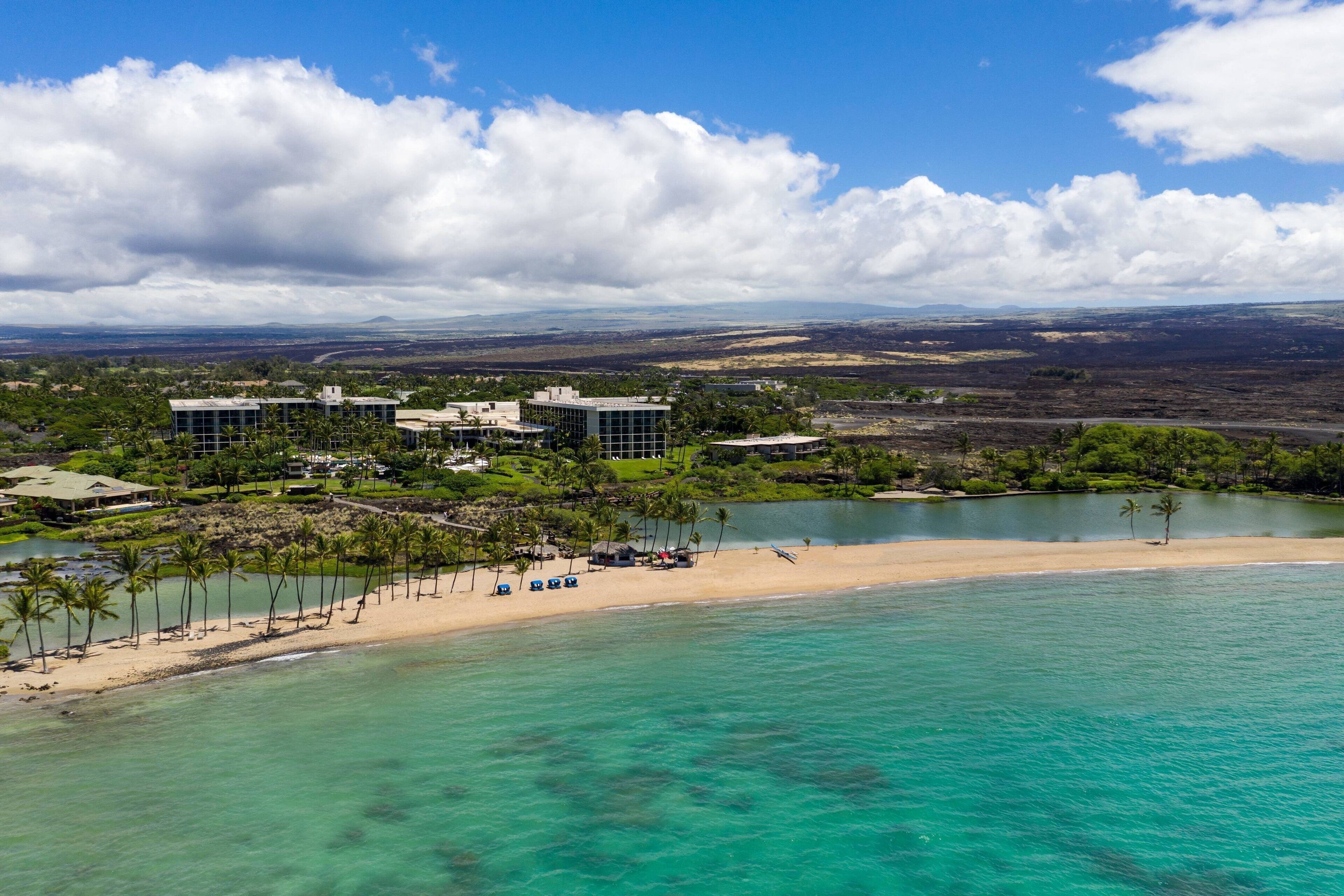 A coastal resort with a beach, clear turquoise waters, and a view of distant mountains.