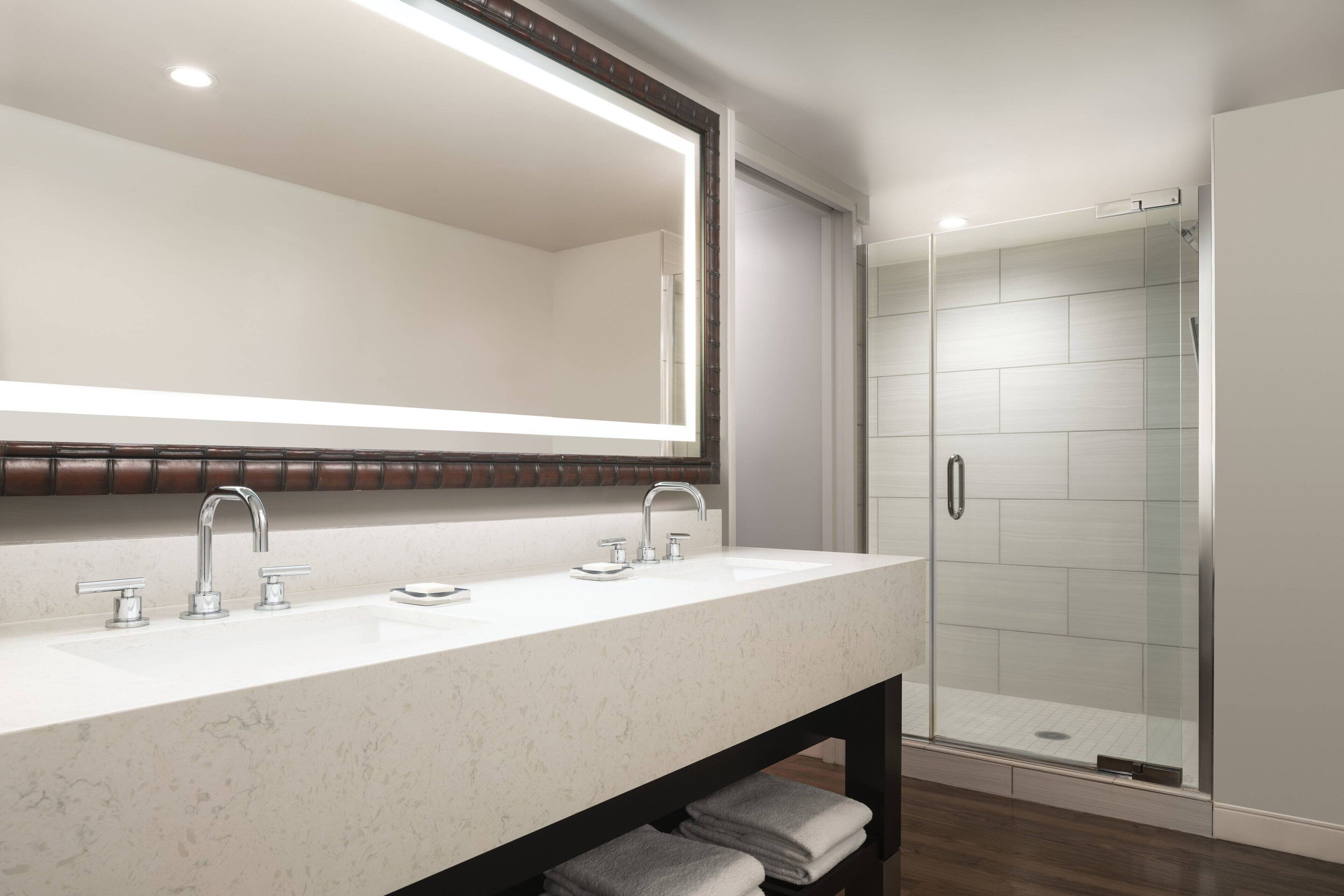 Un baño moderno con un espejo grande, dos lavamanos y una ducha con cerramiento de vidrio.