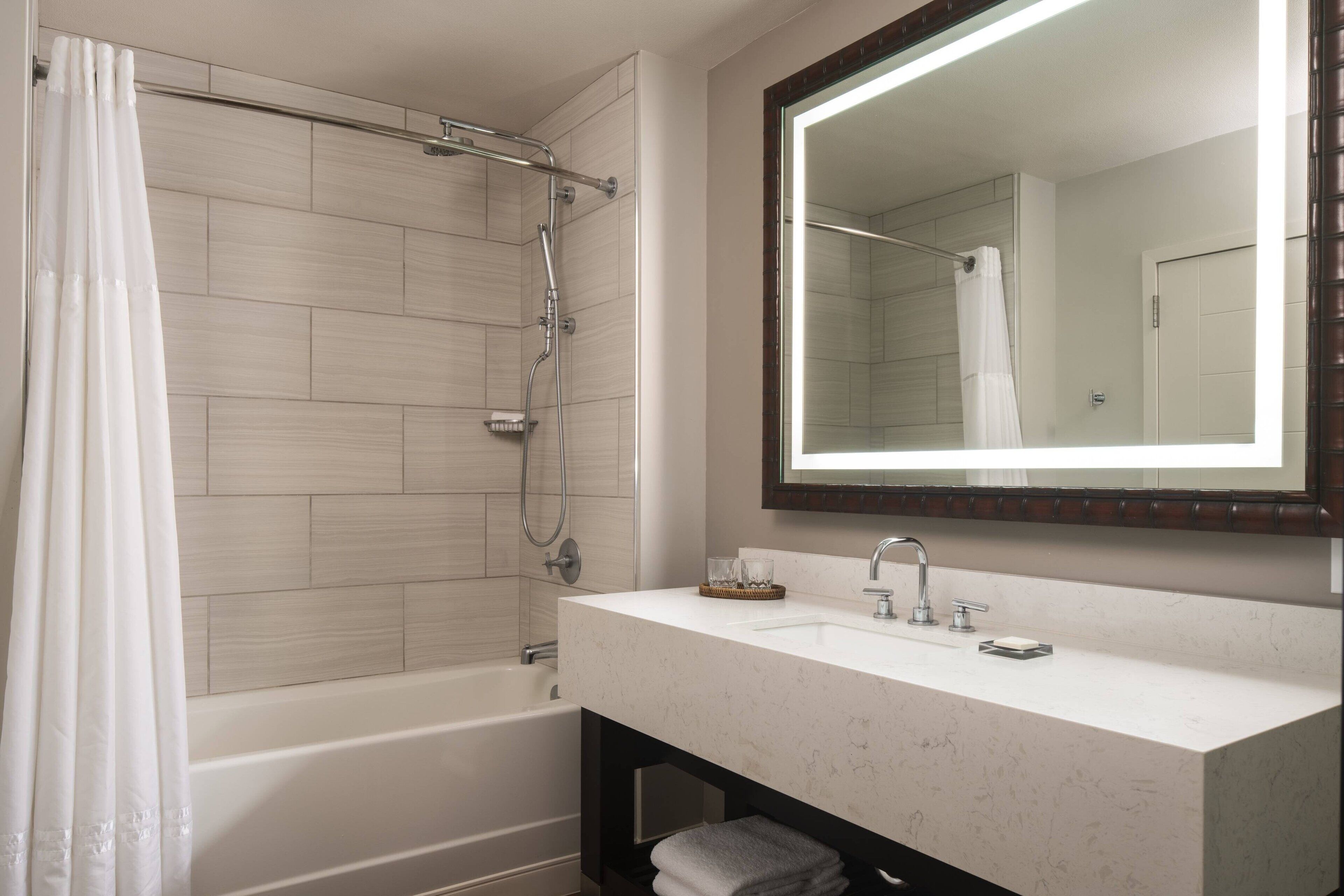 A modern bathroom with a bathtub, shower, and a large mirror above the sink.