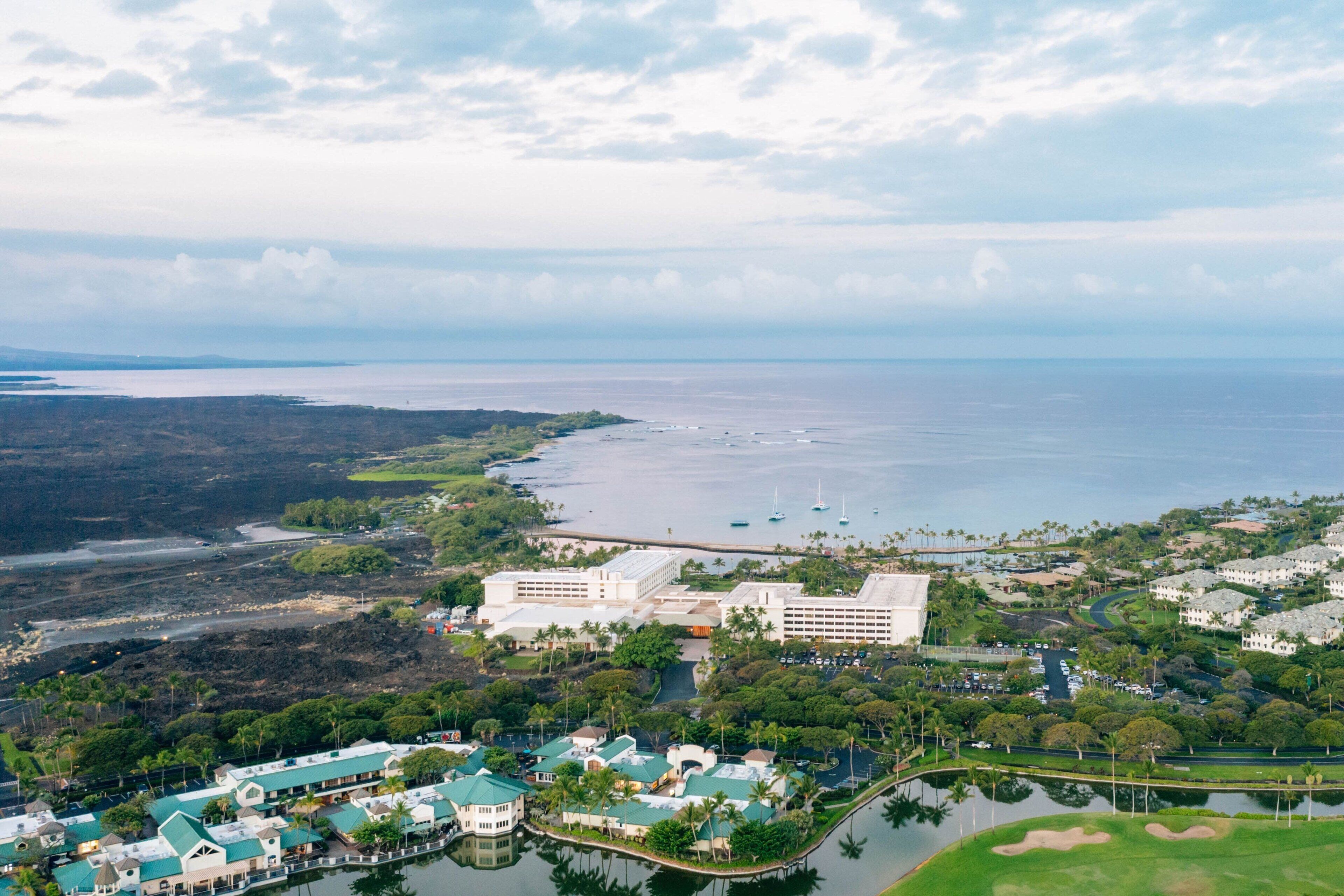 Vista aérea de um resort costeiro com vários edifícios, uma marina e um campo de golfe.