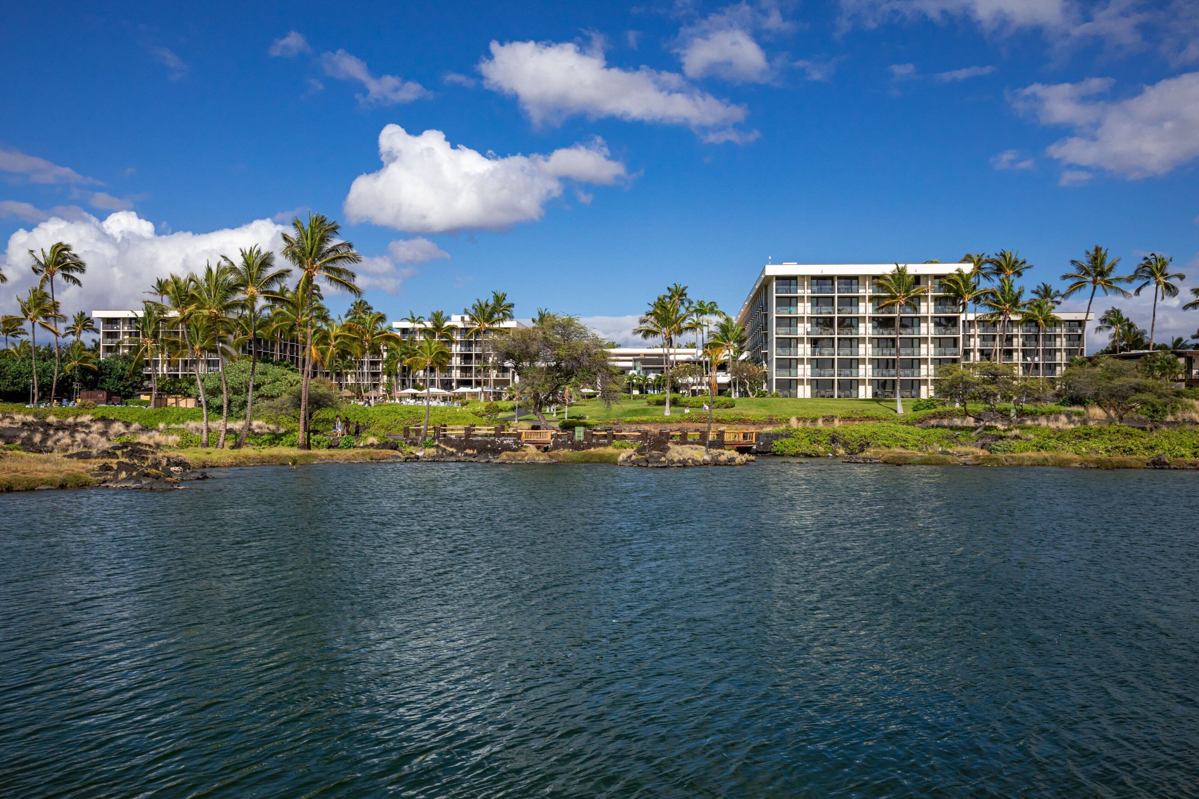 A waterfront hotel with multiple buildings, palm trees, and a clear blue sky.