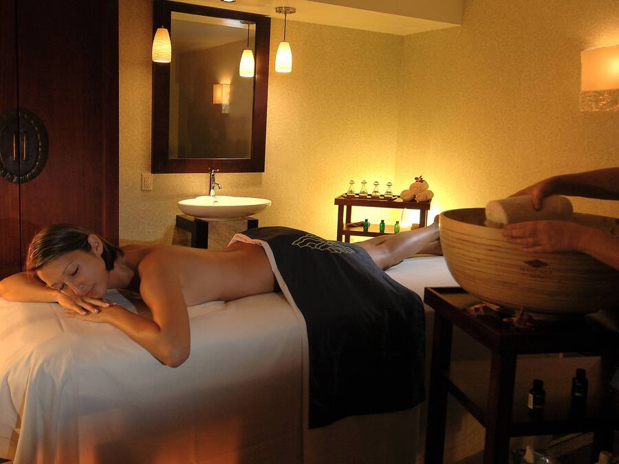 A spa room with a bed, a wooden cabinet, a sink, and a massage table.