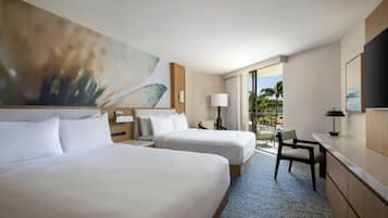 A hotel room with two beds, a desk, a chair, and a view of palm trees.