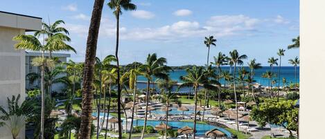 A resort with a pool area, palm trees, and a view of the ocean.