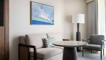A hotel room with a sofa, armchair, round table, and a painting on the wall.