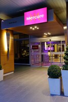 El exterior de un hotel Mercure con un llamativo letrero rosa, puertas de vidrio y una fachada moderna.
