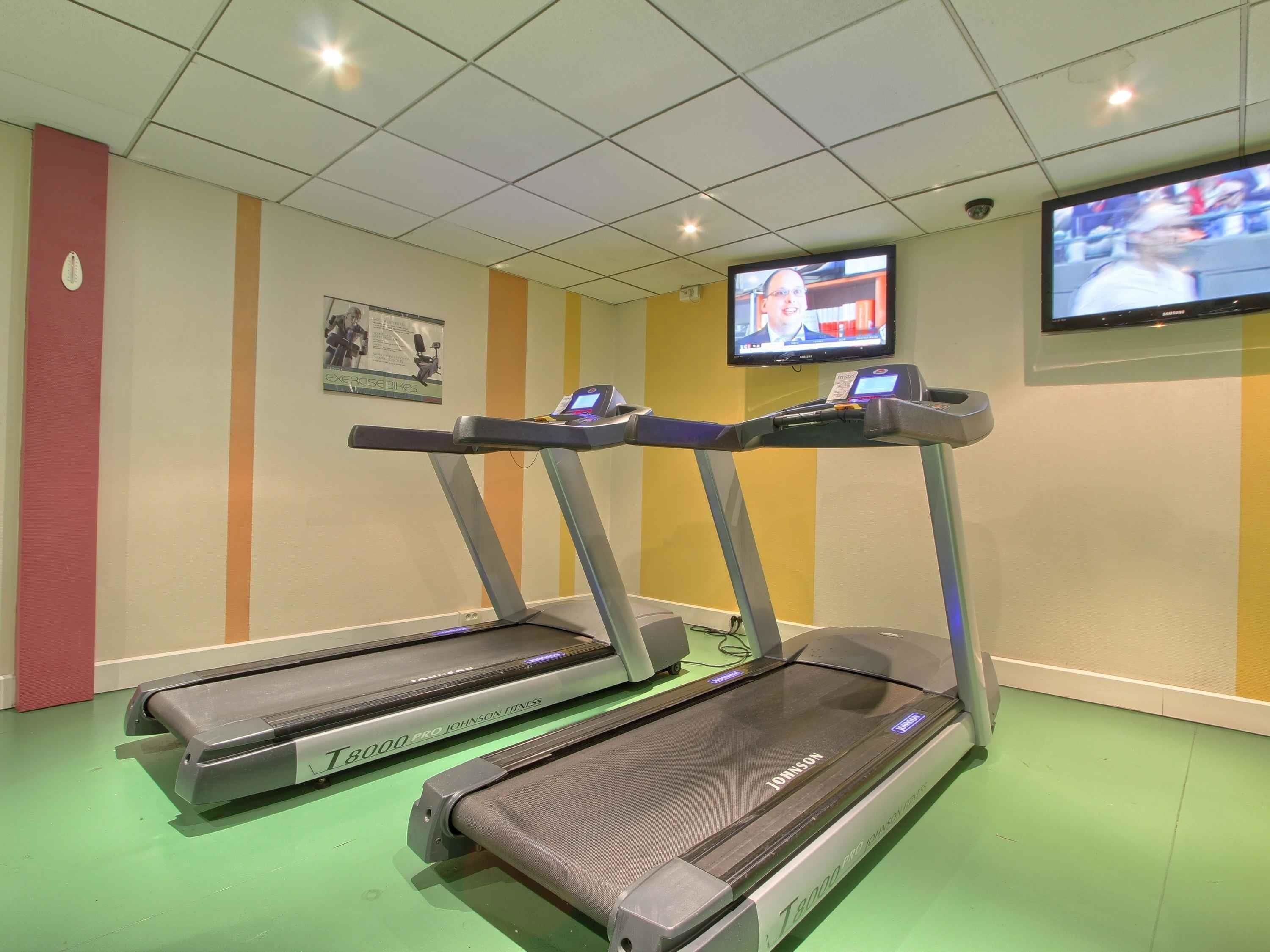 A fitness room with treadmills and a TV mounted on the wall.