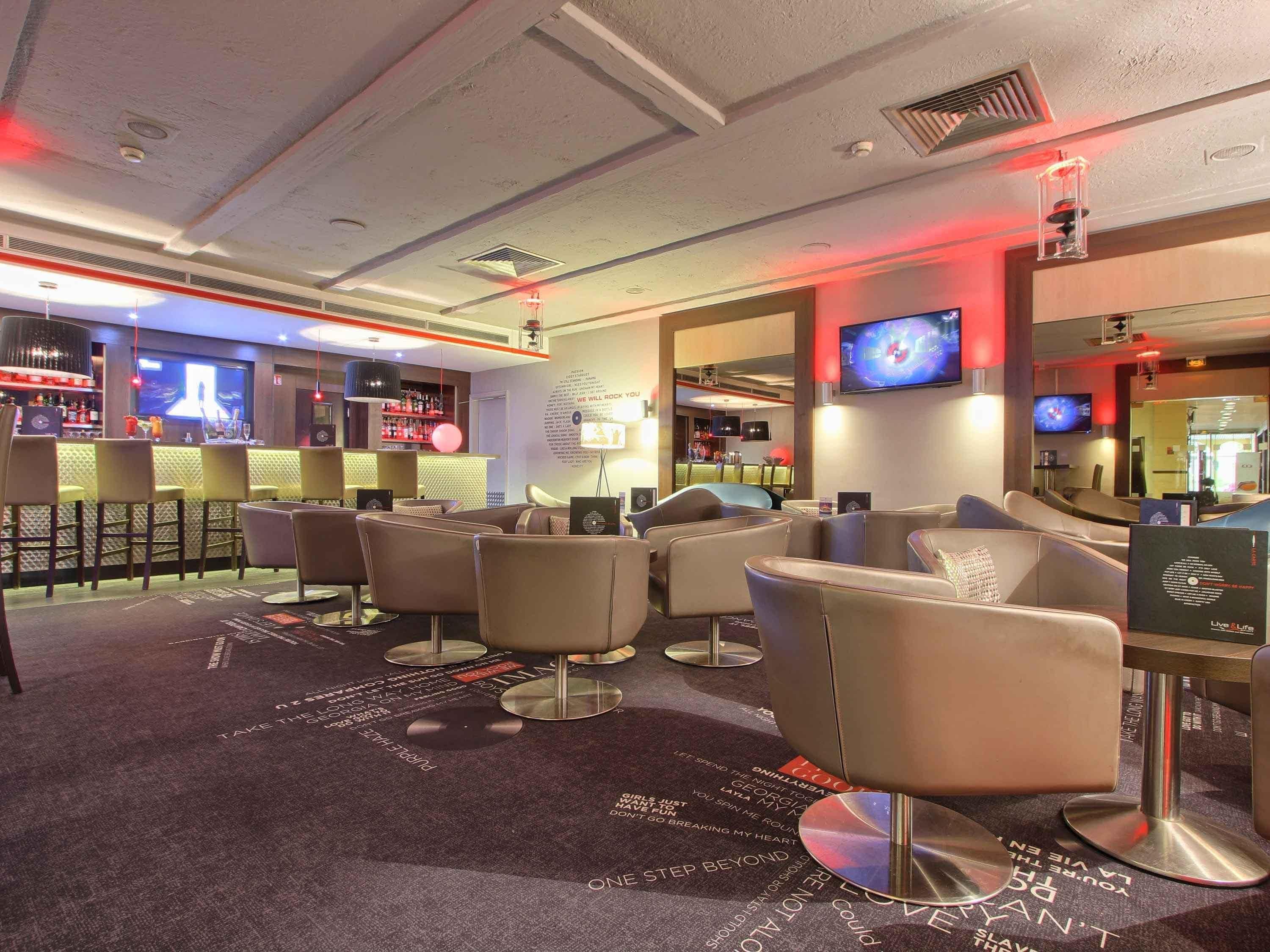 A modern bar area with seating and a bar counter, featuring a television screen and ambient lighting.