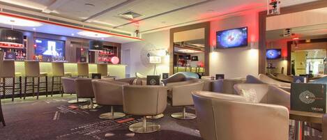 A modern bar area with seating and a bar counter, featuring a television screen and ambient lighting.