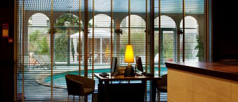 Ein modernes Zimmer mit Schreibtisch, Stühlen und einem großen Fenster mit Blick auf einen Pool und Grünflächen.