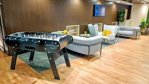 A modern living room with a foosball table, a grey sofa, and a television mounted on the wall. - Mercure Paris Velizy (Velizy-Villacoublay)