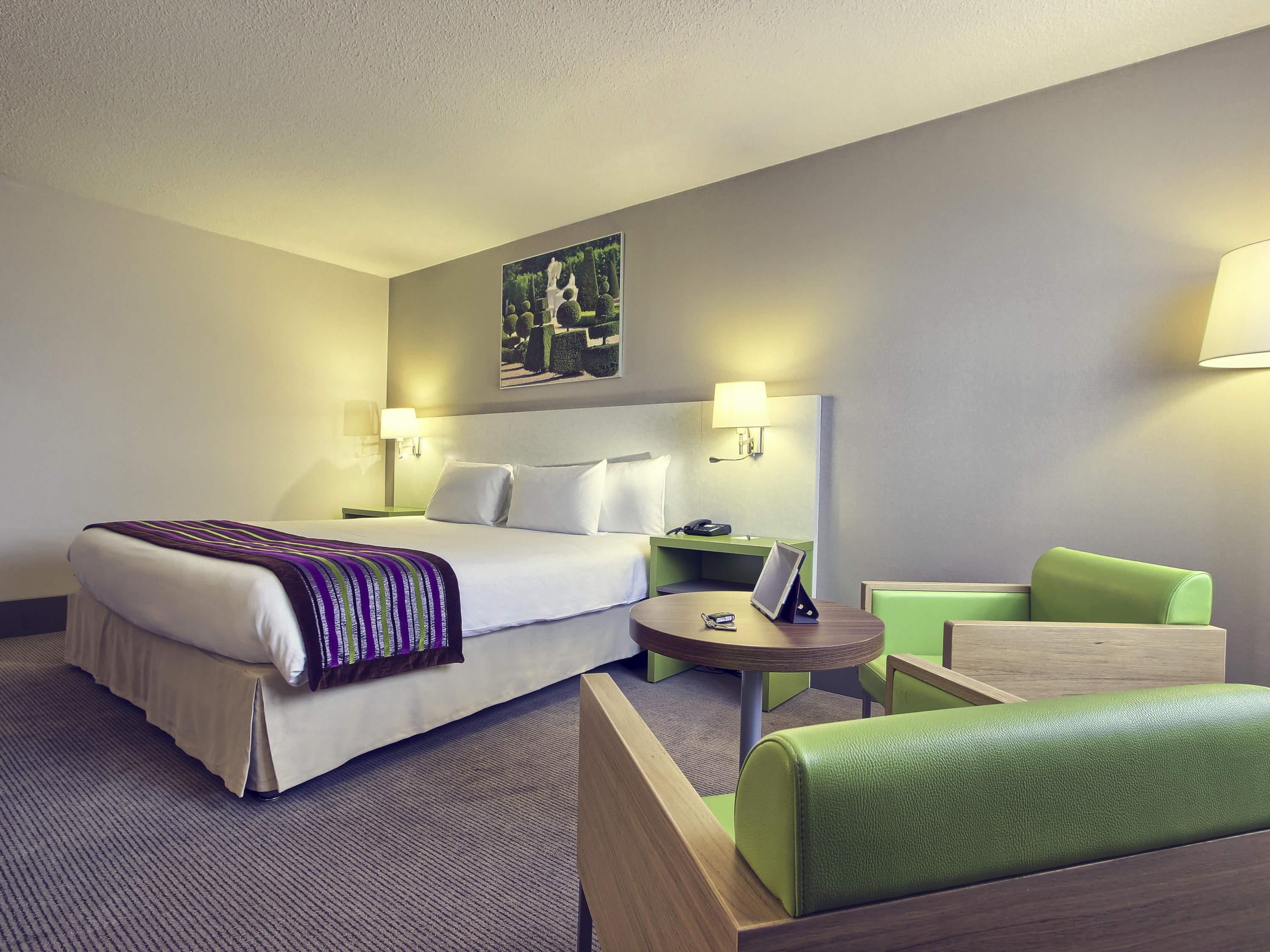 A hotel room with a large bed, bedside tables, a desk, and a green sofa.