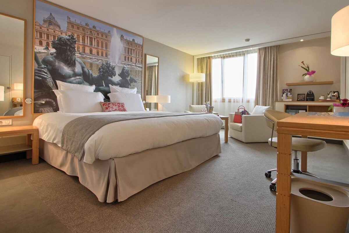 Une chambre d’hôtel avec un grand lit, un bureau, une chaise, une petite table et une grande fenêtre.