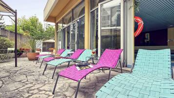Des fauteuils de jardin avec une structure en métal et des assises en fibres tressées, une terrasse en pierre et un bâtiment doté de grandes fenêtres et d’une entrée abritée.