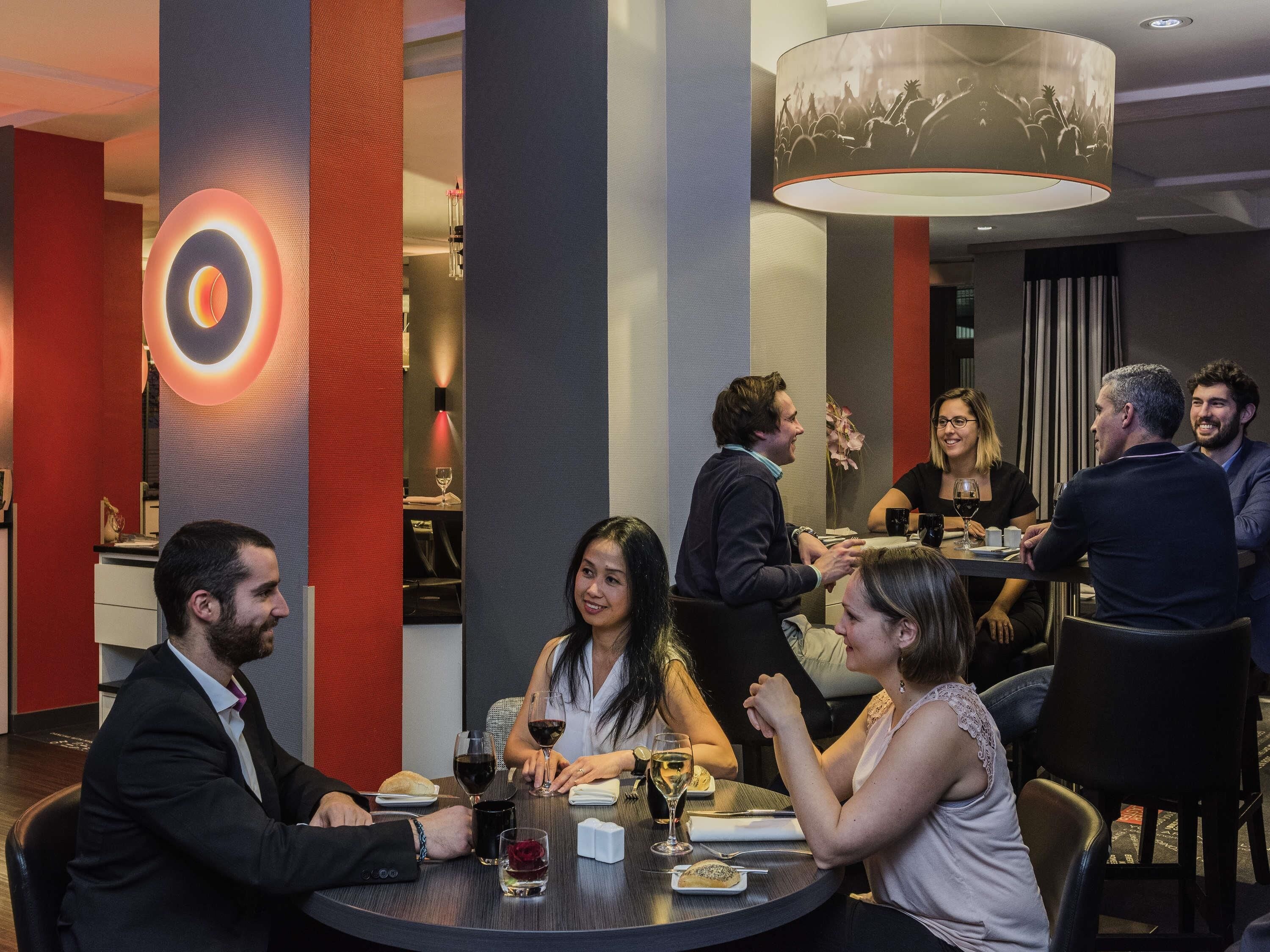 Un grupo de personas cenando en un restaurante moderno con un elemento de iluminación circular central y una araña.