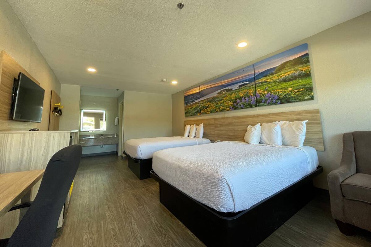 A hotel room with two beds, a desk, a chair, a TV, and a painting on the wall.