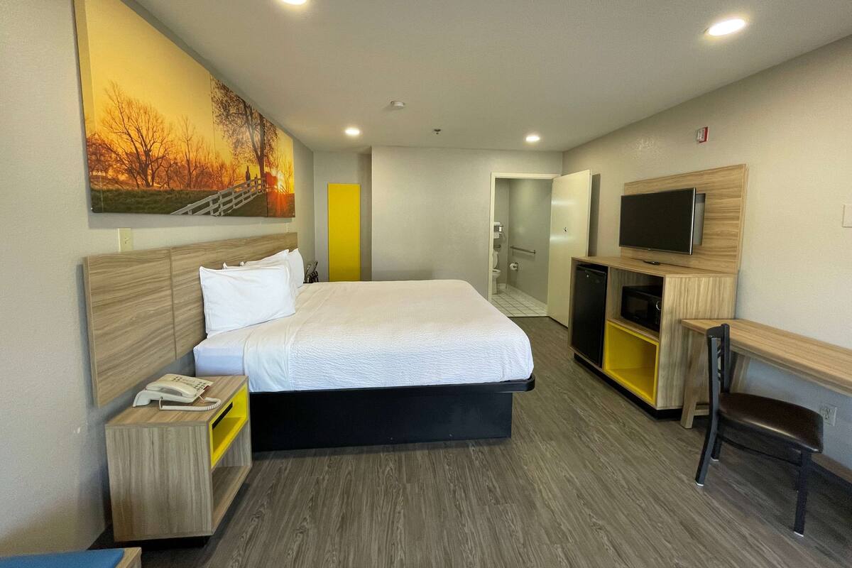 A hotel room with a bed, bedside table, TV, and a painting on the wall.