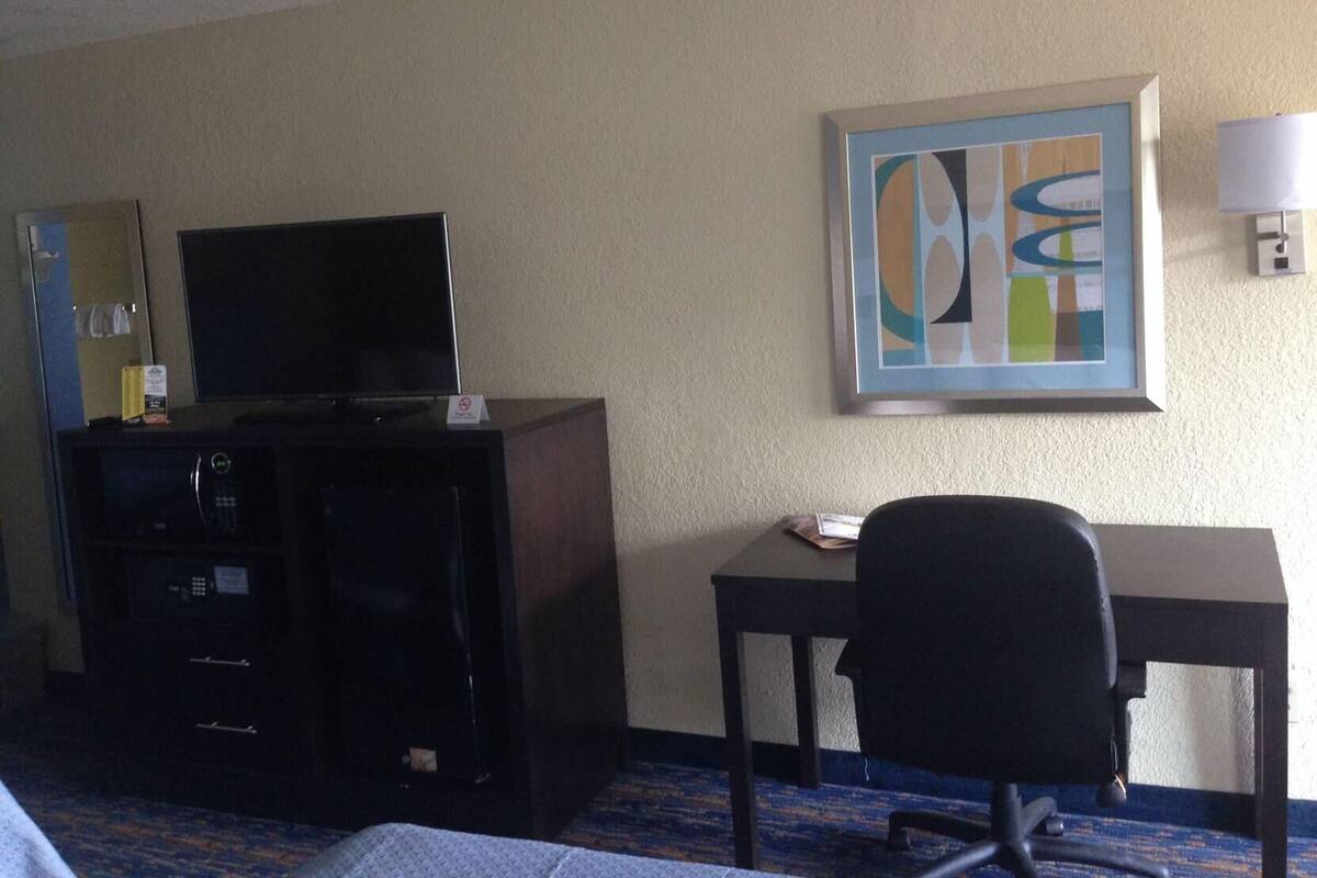 A hotel room with a television on a cabinet, a desk with a chair, and a framed abstract painting on the wall.