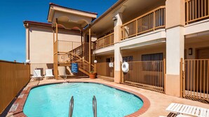A pool area with a clear blue pool, a staircase leading to a balcony, and white lounge chairs. - Days Inn by Wyndham Near Seaworld San Antonio (San Antonio)