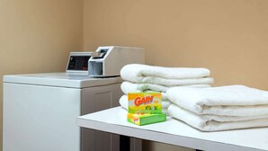 A laundry area with a washing machine, a stack of white towels, and a box of Gain detergent. - Days Inn by Wyndham Near Seaworld San Antonio (San Antonio)