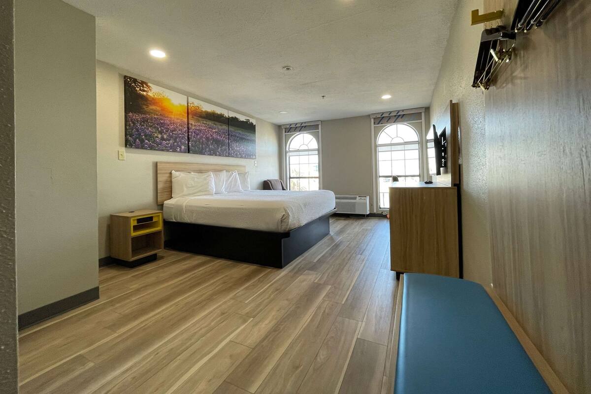 A modern hotel room with a large bed, a bedside table, a bench, and a painting on the wall.