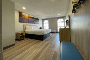 Una habitación de hotel moderna con una cama grande, una mesita de noche, un banco y un cuadro en la pared.