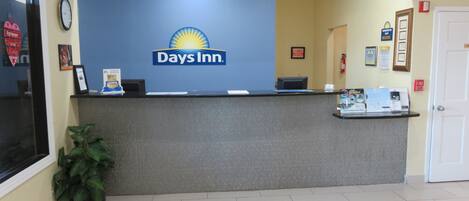 Un mostrador de recepción en un Days Inn, con un reloj, certificados enmarcados y folletos informativos.