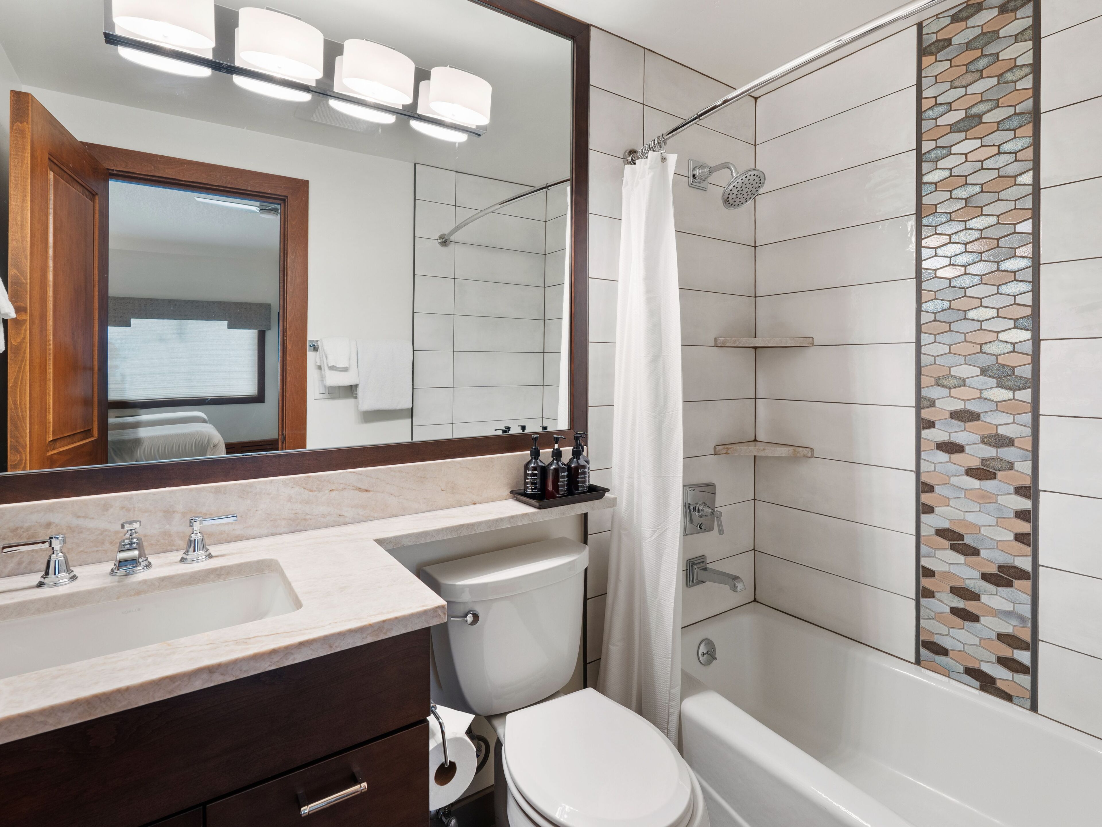 Un baño moderno con lavamanos de mármol, inodoro y ducha con pared de azulejos de vidrio.