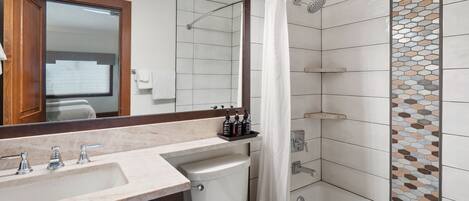 Un baño moderno con lavamanos de mármol, inodoro y ducha con pared de azulejos de vidrio.
