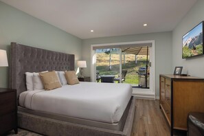 Un dormitorio con una cama grande, una mesita de noche, un aparador y vistas a un patio con mobiliario exterior.
