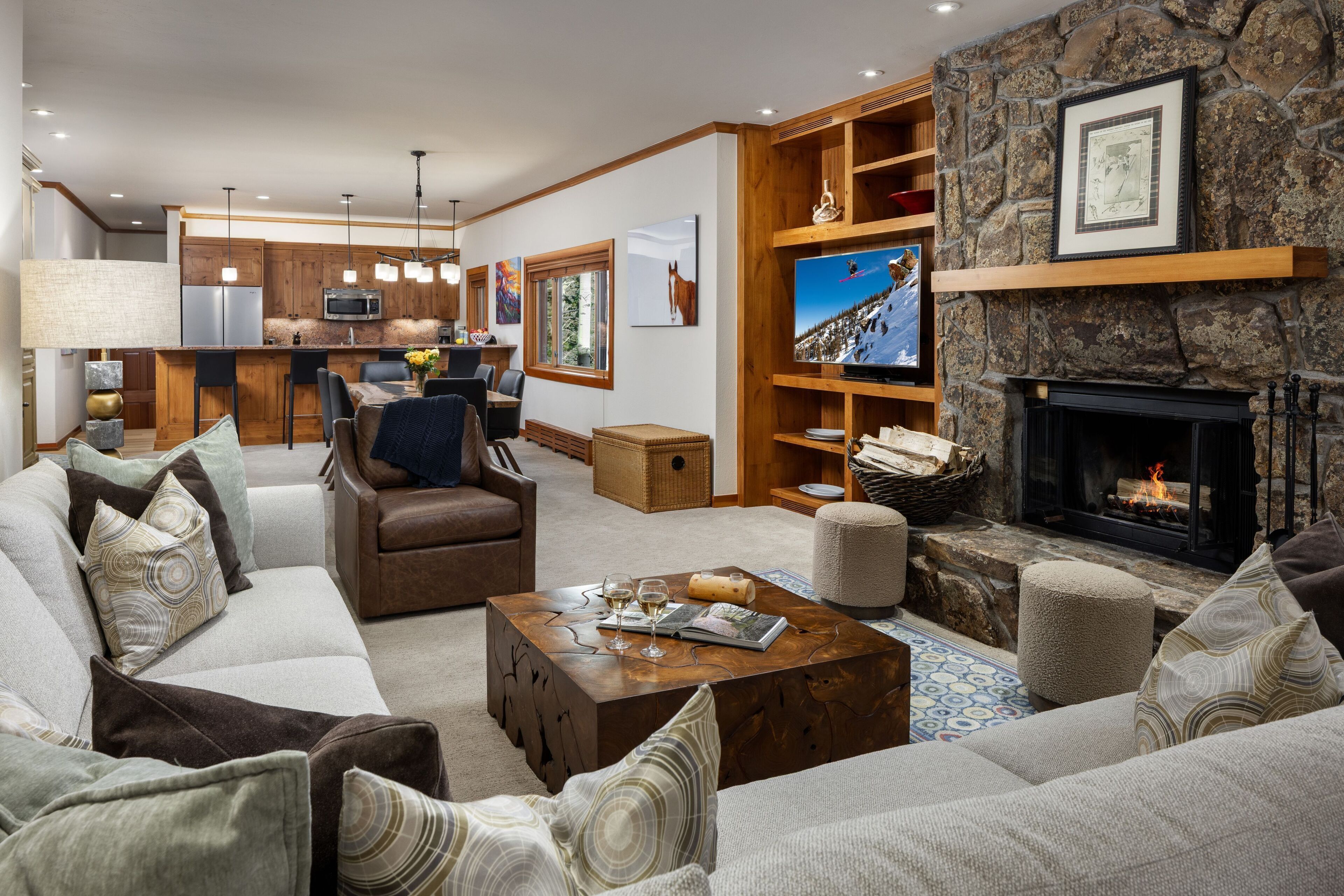 A spacious living room with a fireplace, a kitchen in the background, and a dining area.