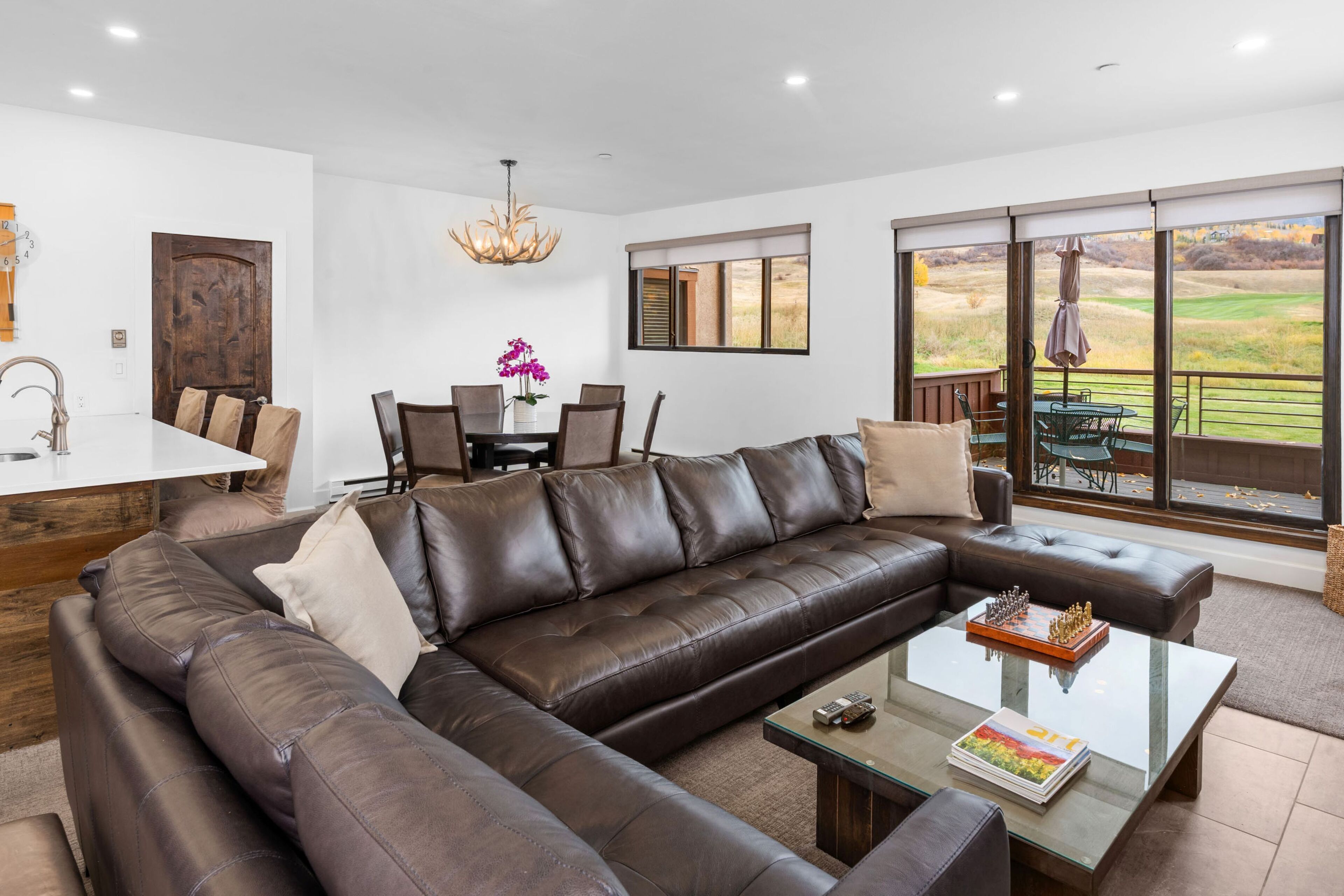 A modern living room with a sectional sofa, a glass coffee table, and a dining area with chairs and a table.