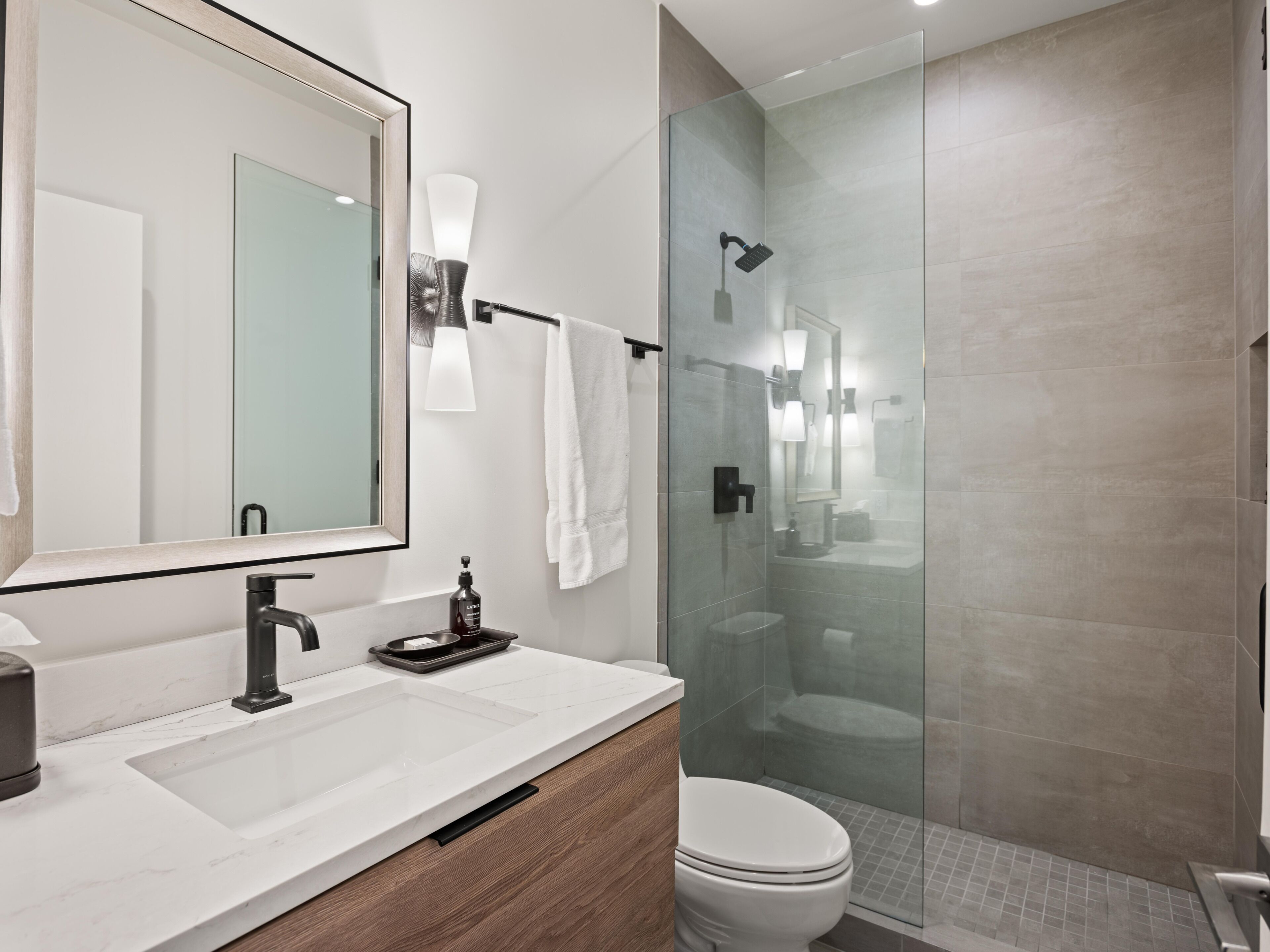 A modern bathroom with a glass-enclosed shower, a white sink with a marble countertop, and a large mirror.