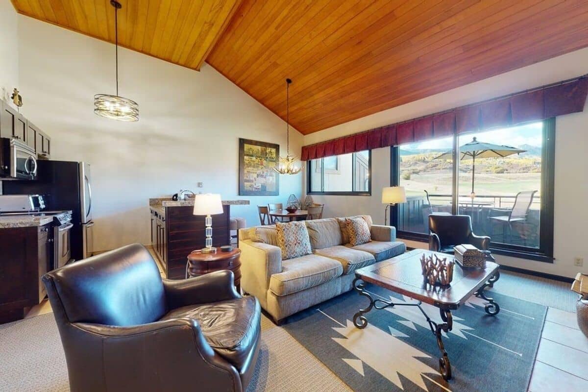 Un amplio espacio de sala con techo de madera, un conjunto de sofás, una mesa de comedor y vistas al exterior.
