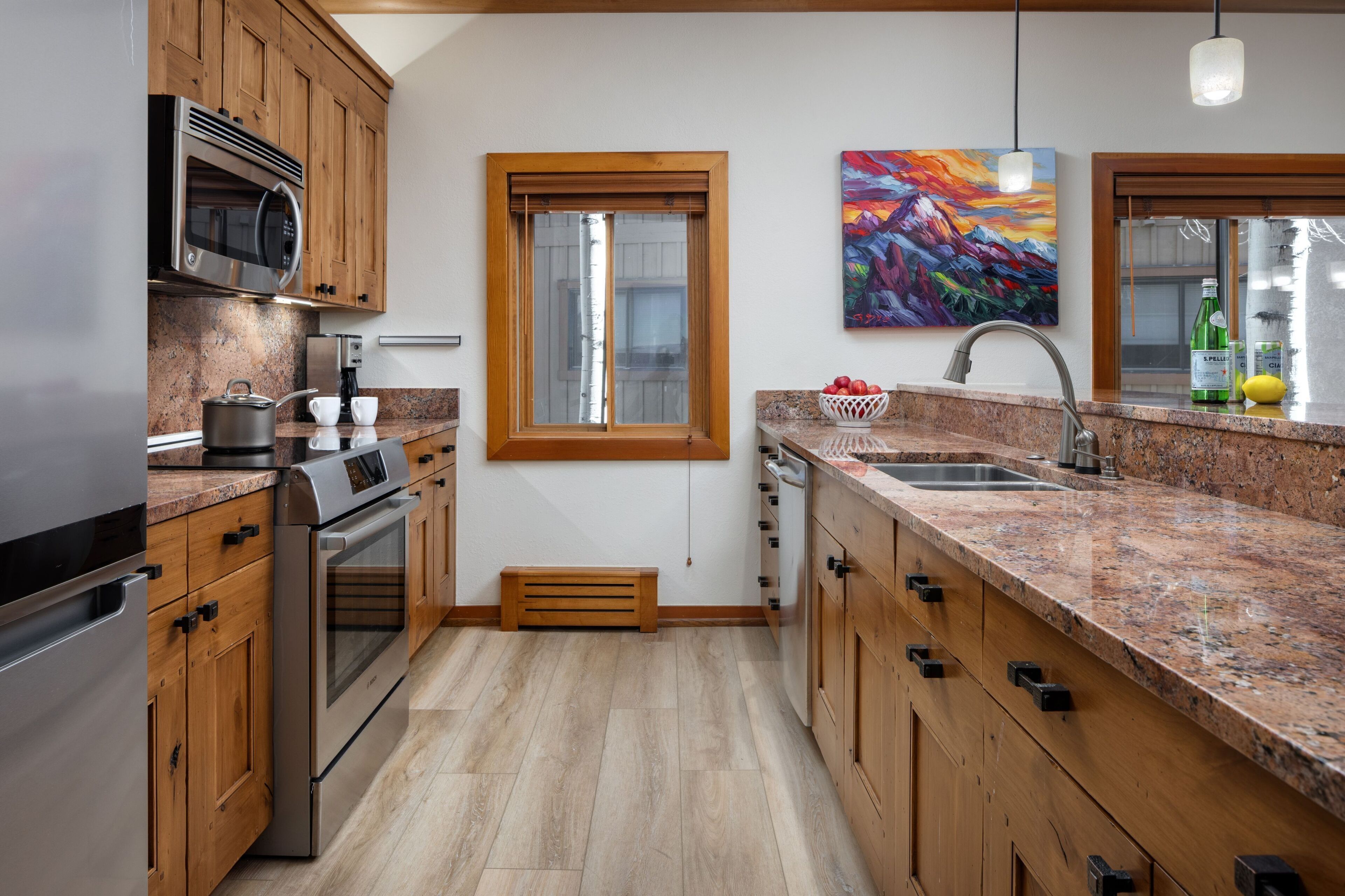 A modern kitchen with wooden cabinets, stainless steel appliances, granite countertops, and a large window.