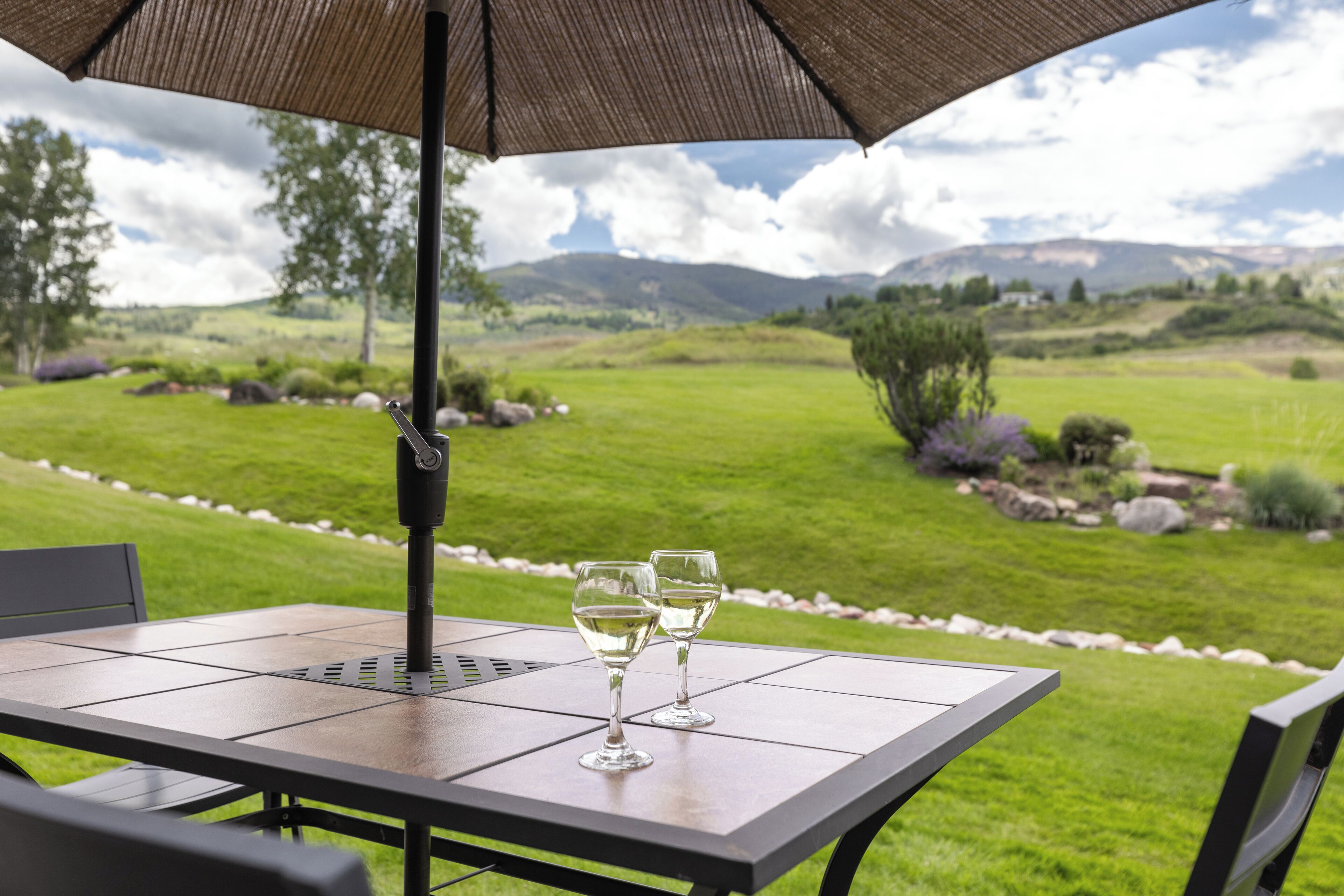 Un patio exterior con una mesa, dos copas de vino y una sombrilla.