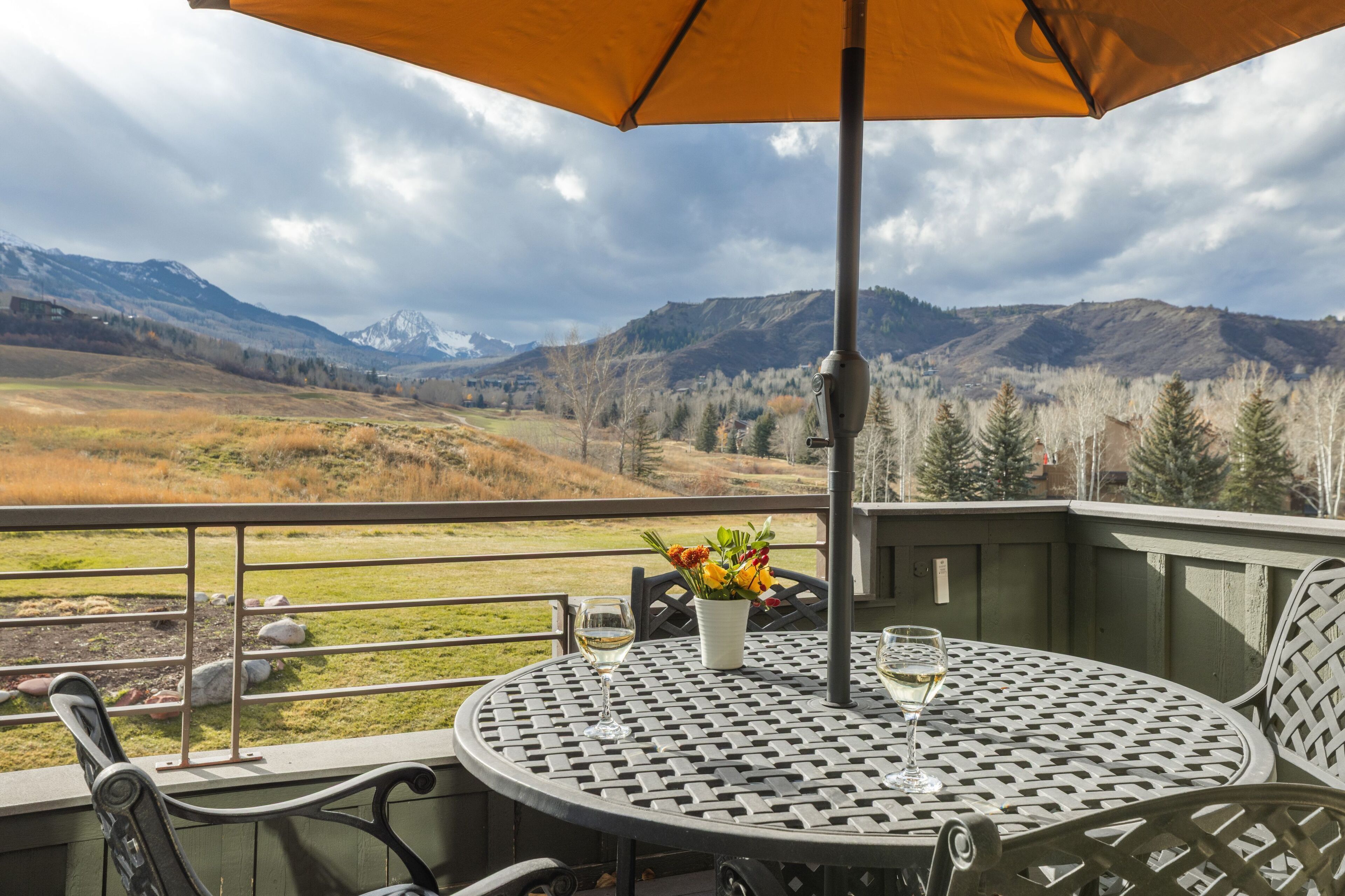 A balcony with a table, chairs, and an umbrella overlooking a mountainous landscape.