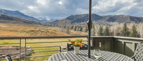 A balcony with a table, chairs, and an umbrella overlooking a mountainous landscape.