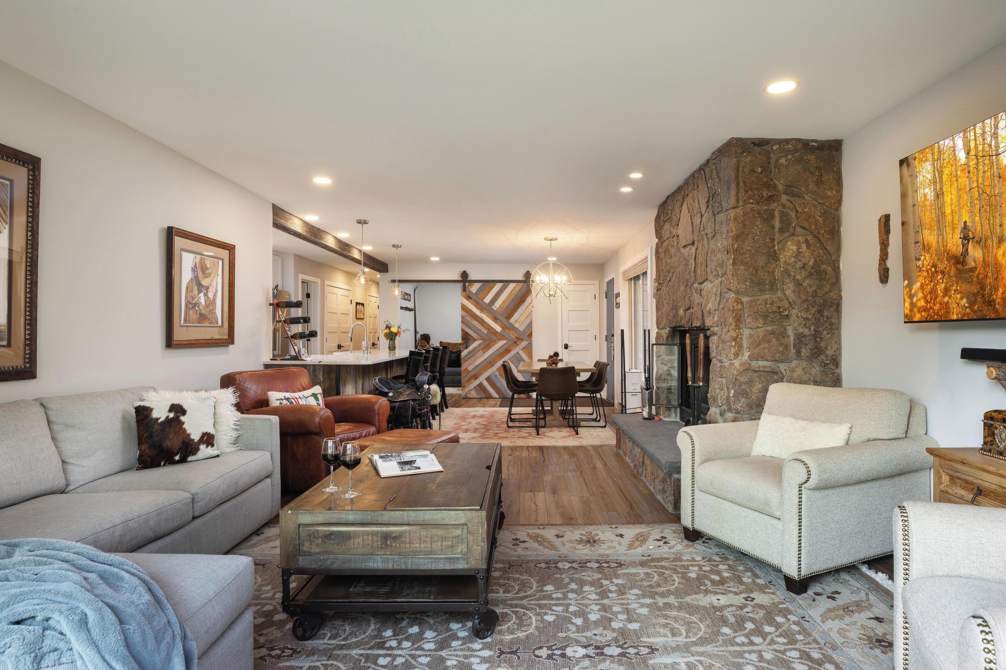 A spacious living room with a fireplace, a dining area, and a kitchen in the background.