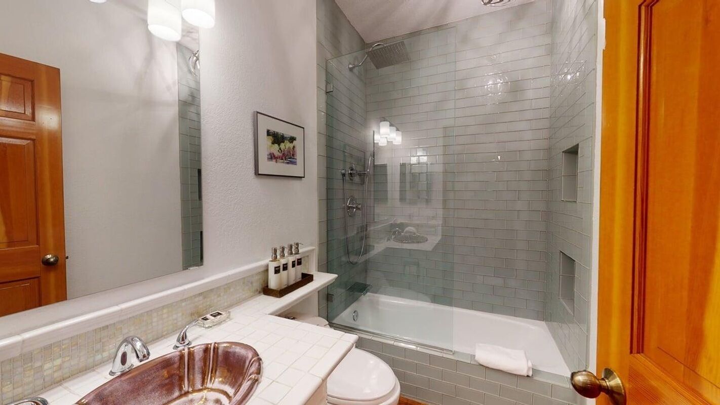 A bathroom with a glass-enclosed shower, a white sink, and a wooden door.