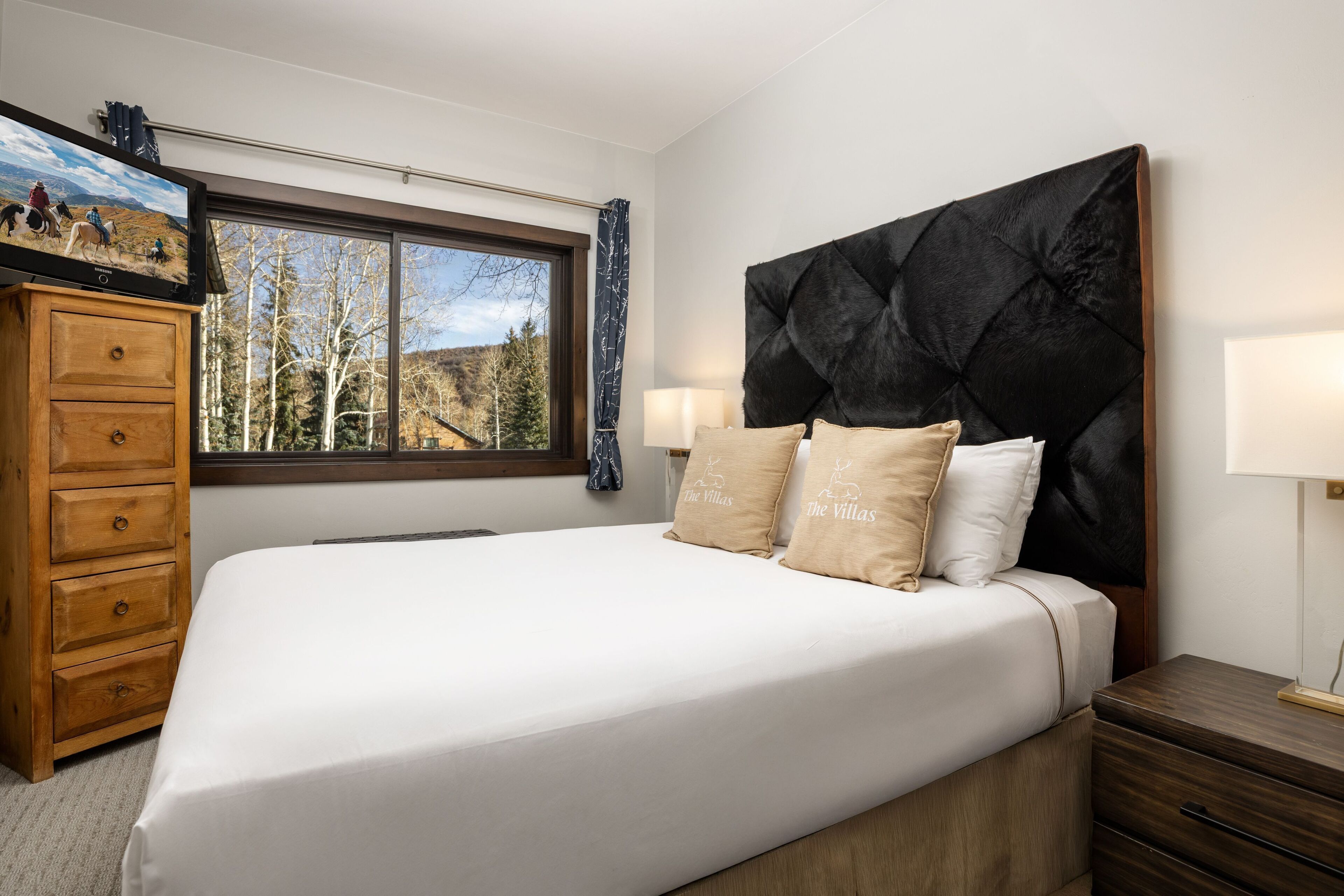 Un dormitorio con una cama grande, un aparador de madera y una ventana con vistas a árboles y montañas.