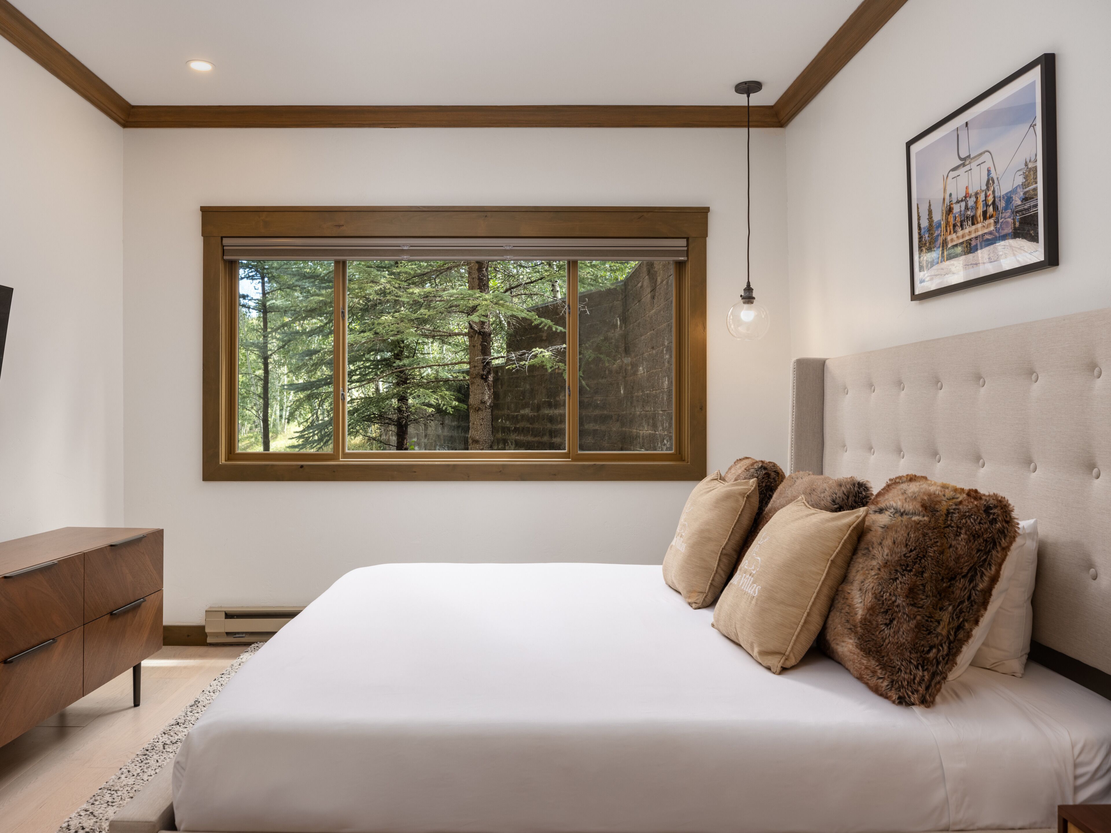 A bedroom with a large window, a bed with white linens, a headboard, and a framed picture on the wall.