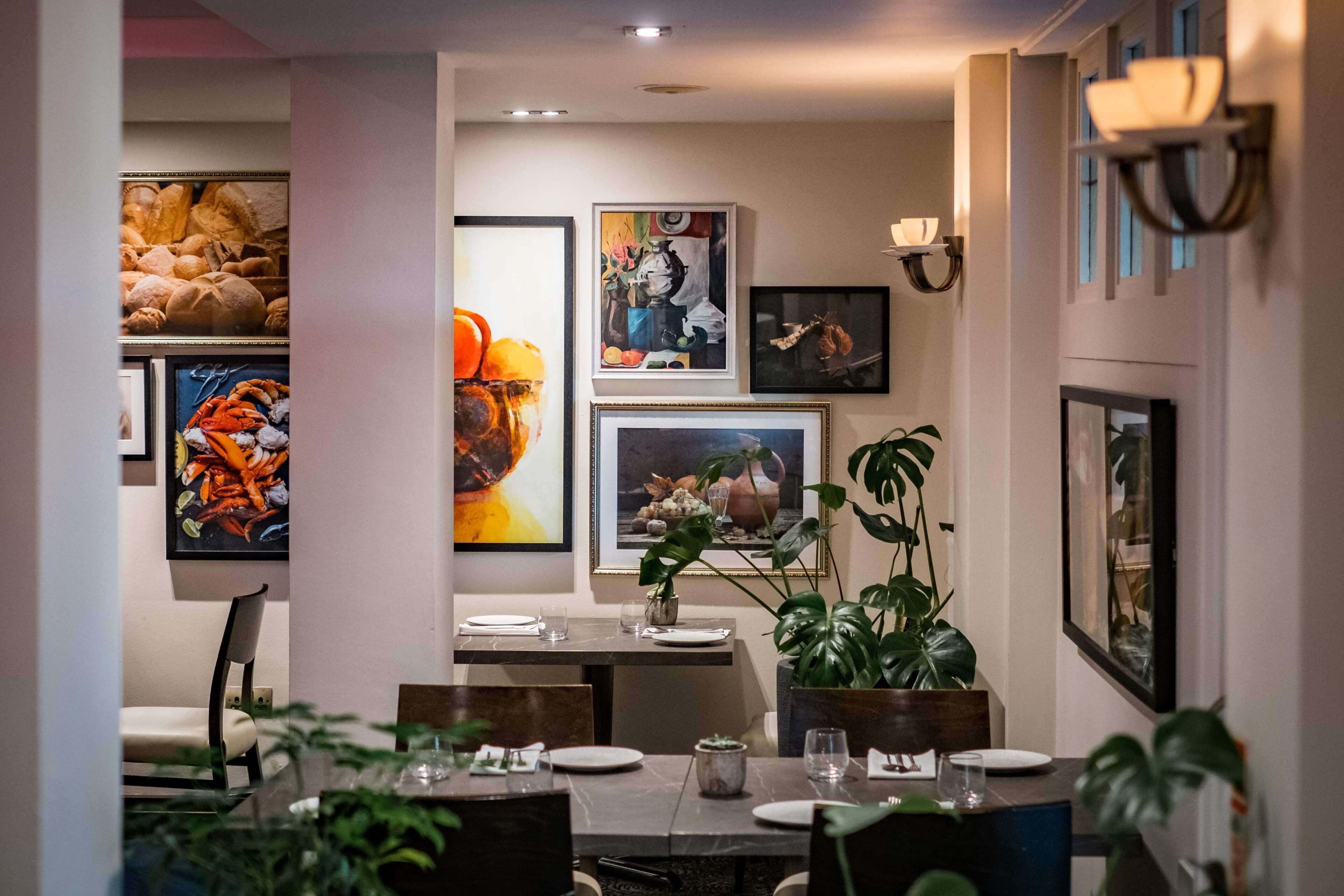 A dining area with a table set for two, surrounded by framed artwork on the walls.