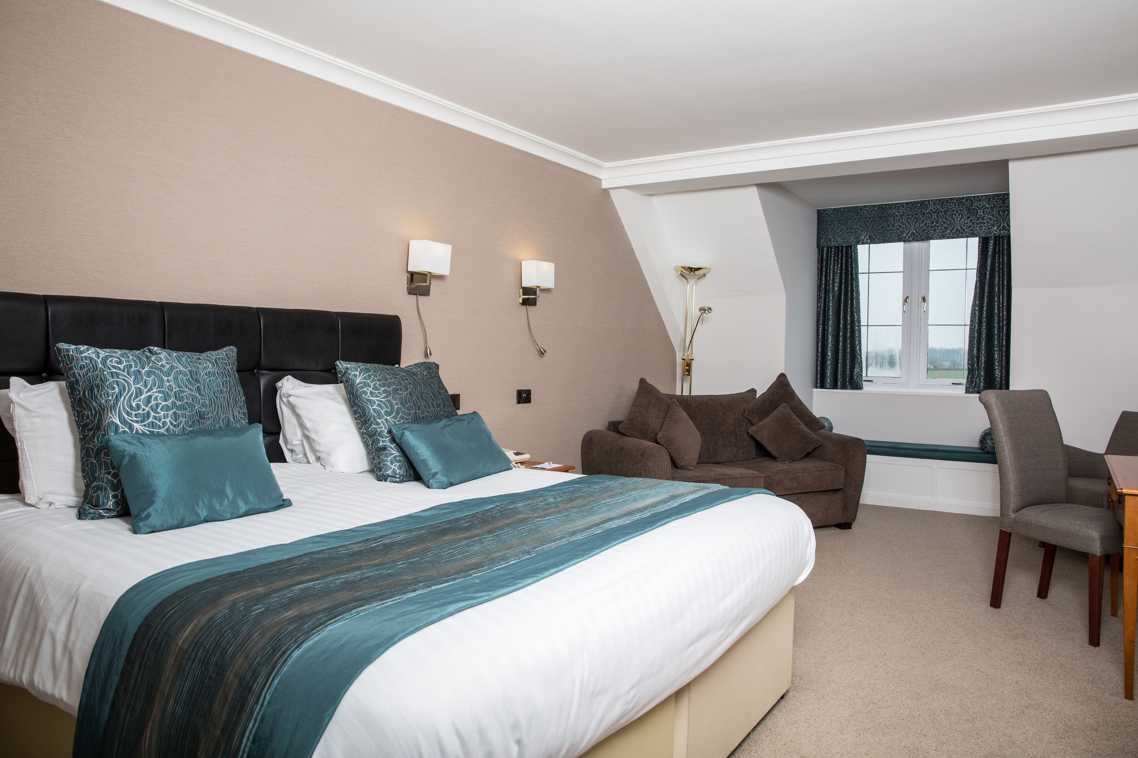 A hotel room with a large bed, a sofa, a chair, and a window with curtains.