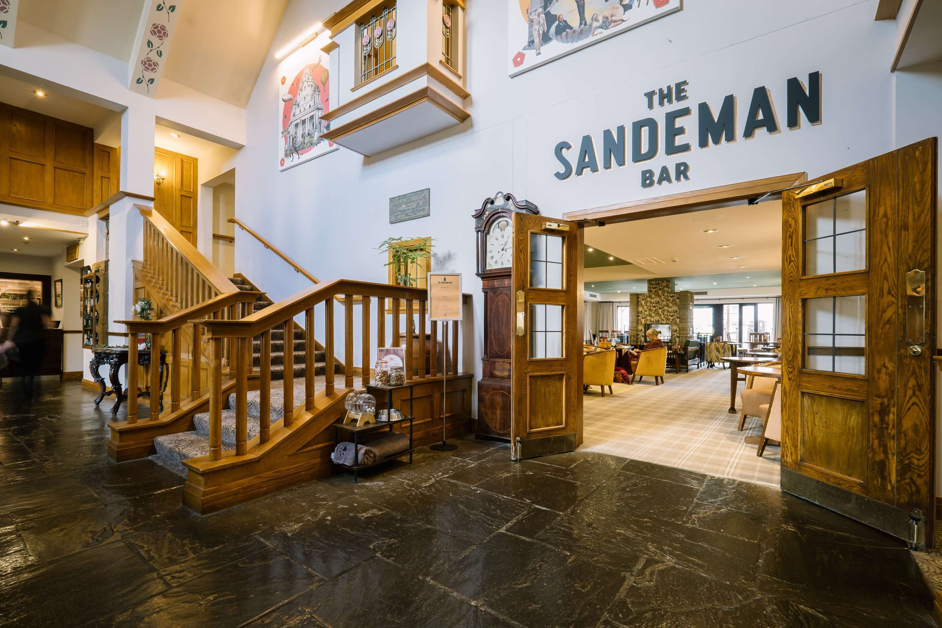 A bar area with a staircase leading to upper floors, wooden doors, and a stone floor.