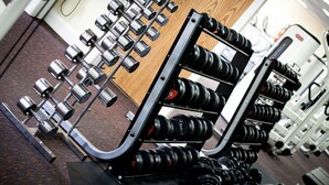 Uma academia com equipamentos de musculação, incluindo halteres e barras.