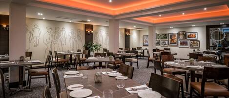 A restaurant with multiple dining tables, chairs, and a ceiling with orange lighting.