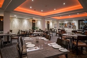 A restaurant with multiple dining tables, chairs, and a ceiling with orange lighting.