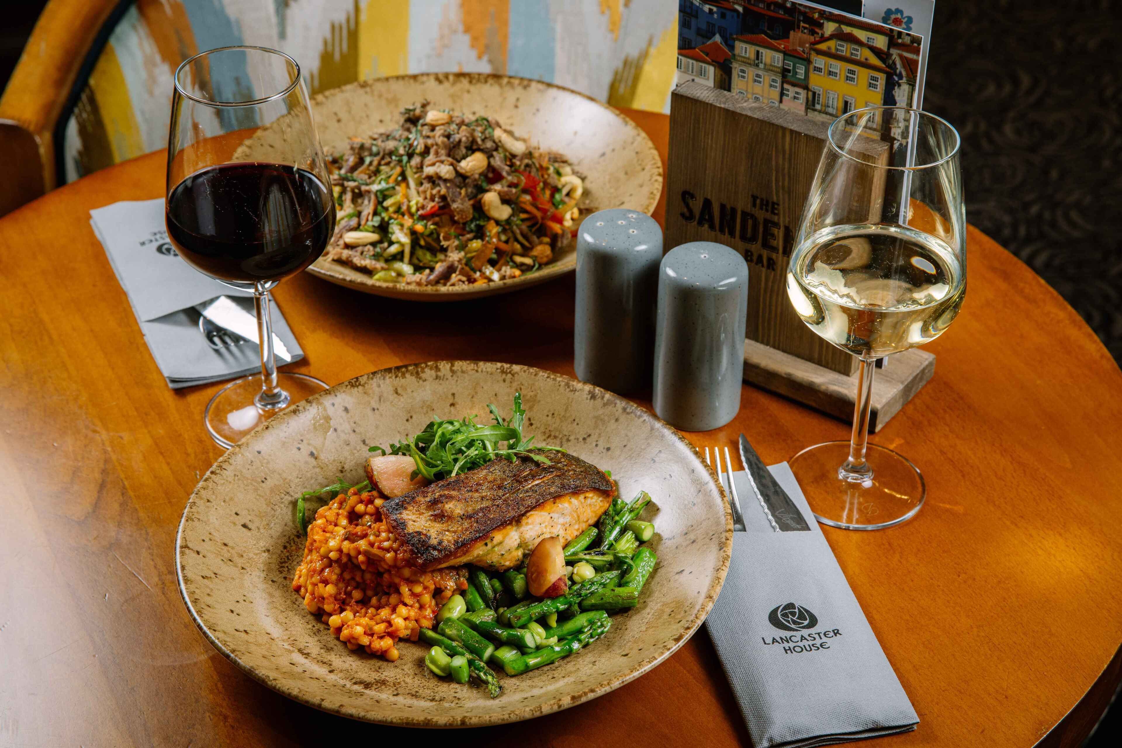 A dining table with a plate of food, two glasses of wine, and salt and pepper shakers.