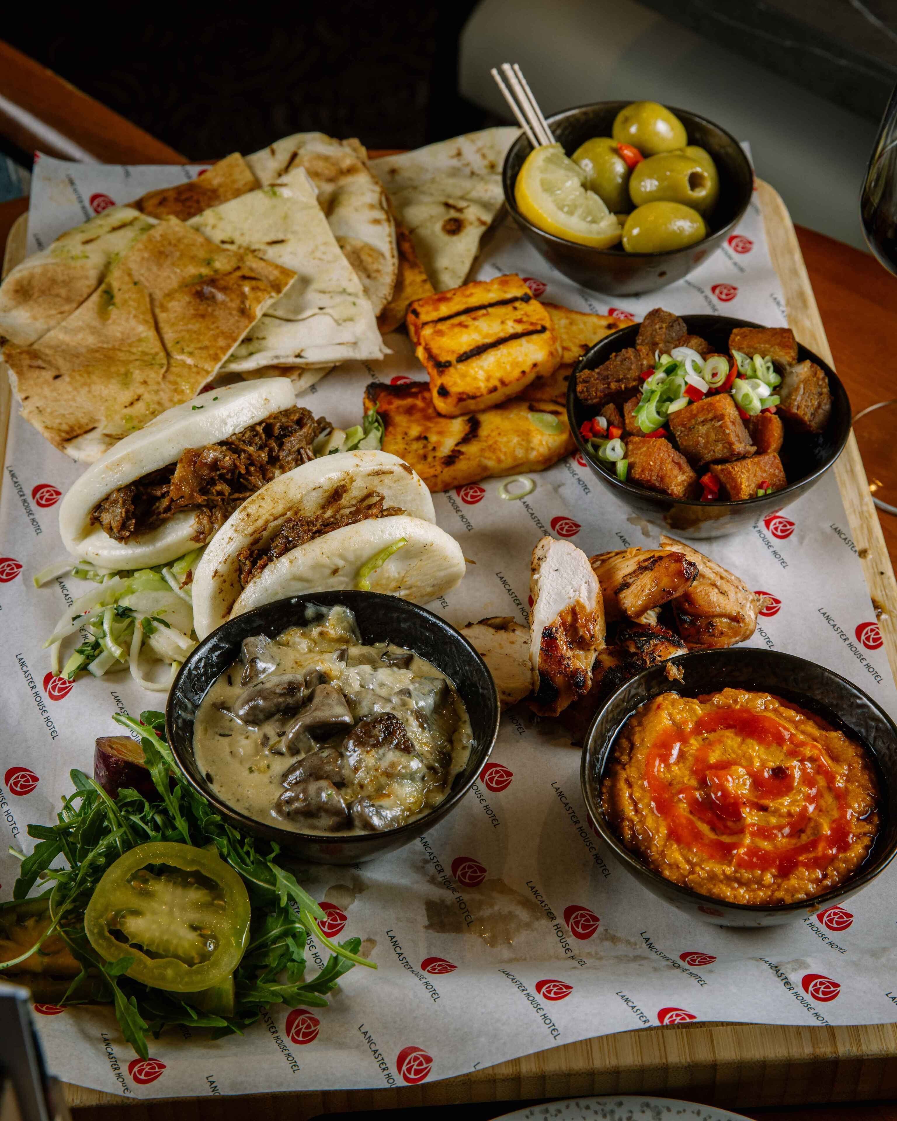 Une variété de plats, notamment des tacos, de la viande grillée et des sauces, servis sur une table recouverte d’une nappe en papier à l’effigie de la marque.